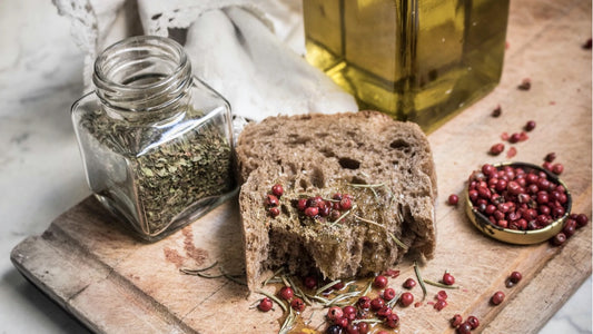 Olive oil drizzled on a piece of thick whole wheat bread with a jar of spices and bottle of olive oil in the background.