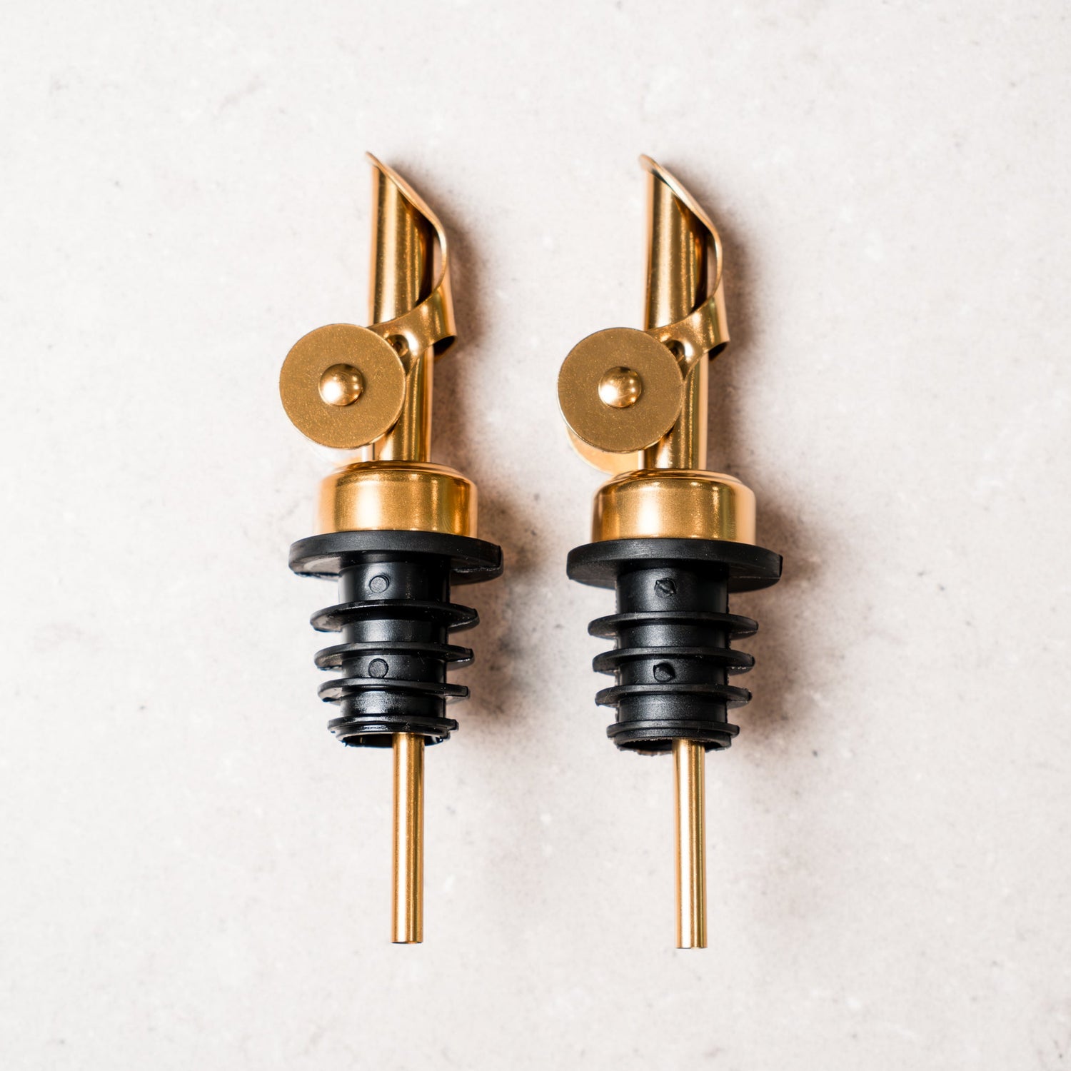 Two gold and black bottle spouts on a light gray background